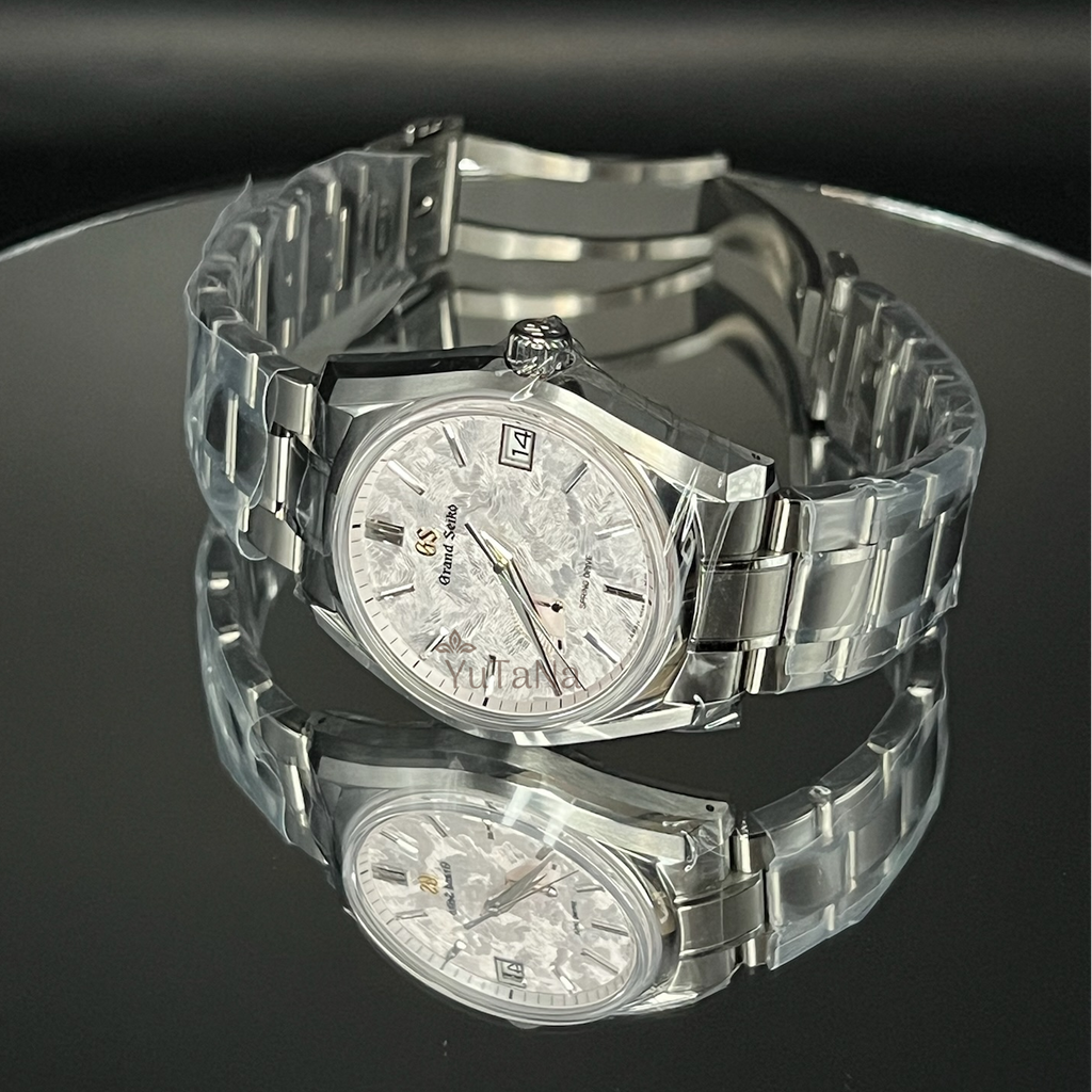 A stainless steel wristwatch with a silver-toned metal link bracelet and a textured white dial, displayed on a reflective black surface.