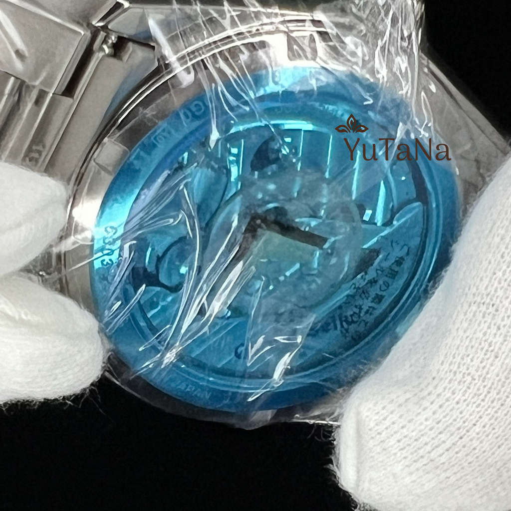 A close-up of a blue metallic watch dial still wrapped in clear plastic