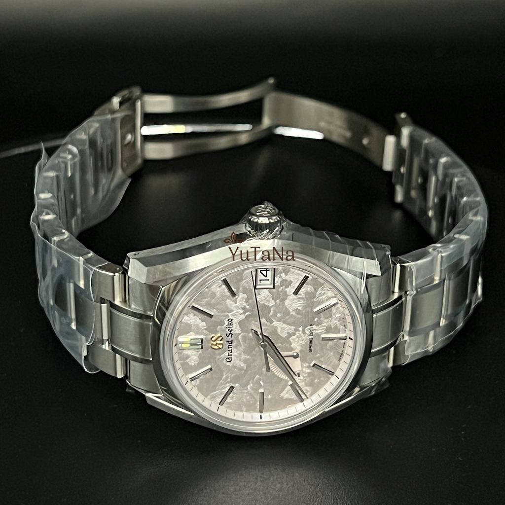 A stainless steel wrist watch with a silver dial and matching metal bracelet, photographed on a dark reflective surface.