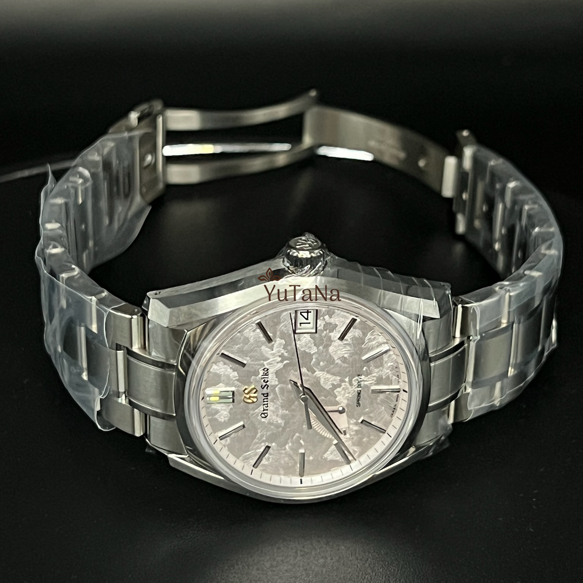 A stainless steel wrist watch with a silver dial and matching metal bracelet, photographed on a dark reflective surface.